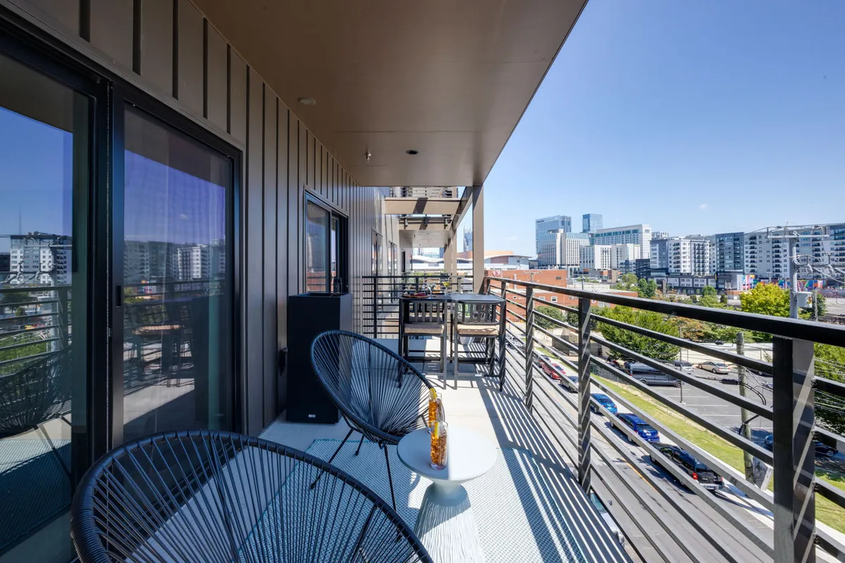 An inviting image of a private balcony featuring comfortable outdoor furniture and railings, overlooking the city skyline. The setting suggests a perfect spot for group meals, morning coffee, or evening relaxation while soaking in urban views.