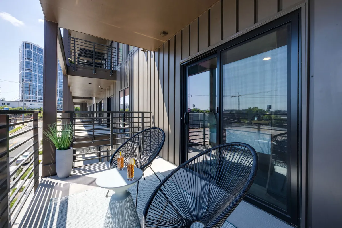 A stylish outdoor seating area with chairs and a small table overlooks a dynamic city view. Potted plants add a touch of tranquility, while the cityscape in the background connects the property to Nashville’s energetic urban environment.