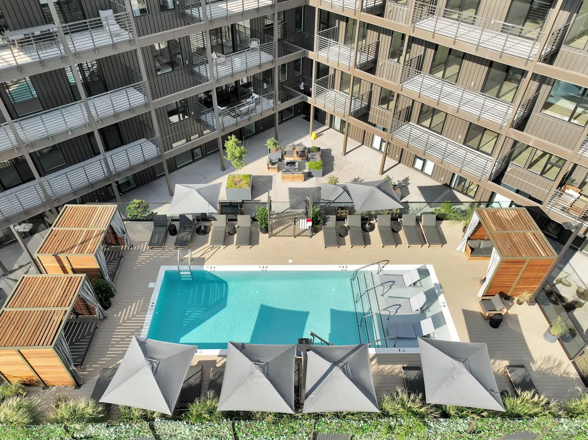 This image showcases a vibrant scene around the resort-style swimming pool, with multiple lounge chairs, shaded cabanas, and an outdoor seating area. Guests are seen swimming, sunbathing, and socializing, all set against a relaxed backdrop that hints at morning yoga sessions, sunset gatherings, and weekend barbecues.