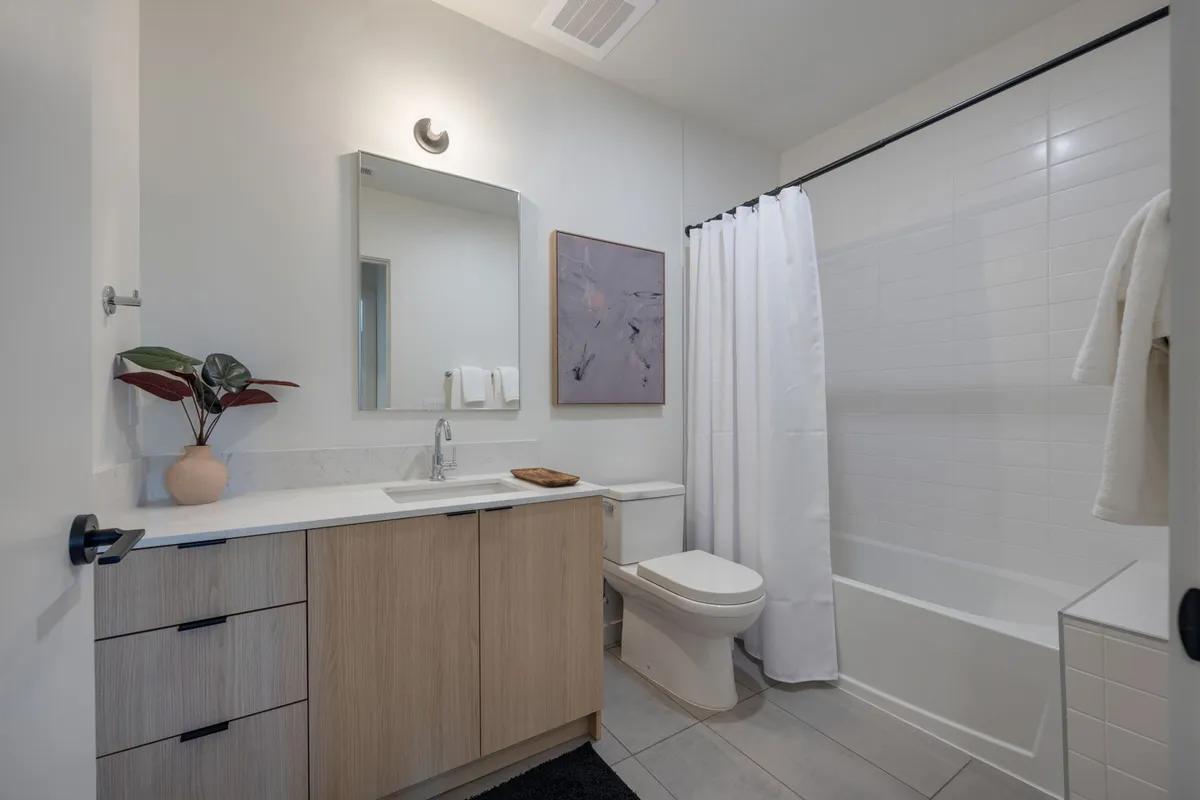 A stylish bathroom vanity with wooden cabinetry, a large mirror, and a decorative plant in a vase. The space exudes a fresh and calming atmosphere, ideal for self-care and daily routines.