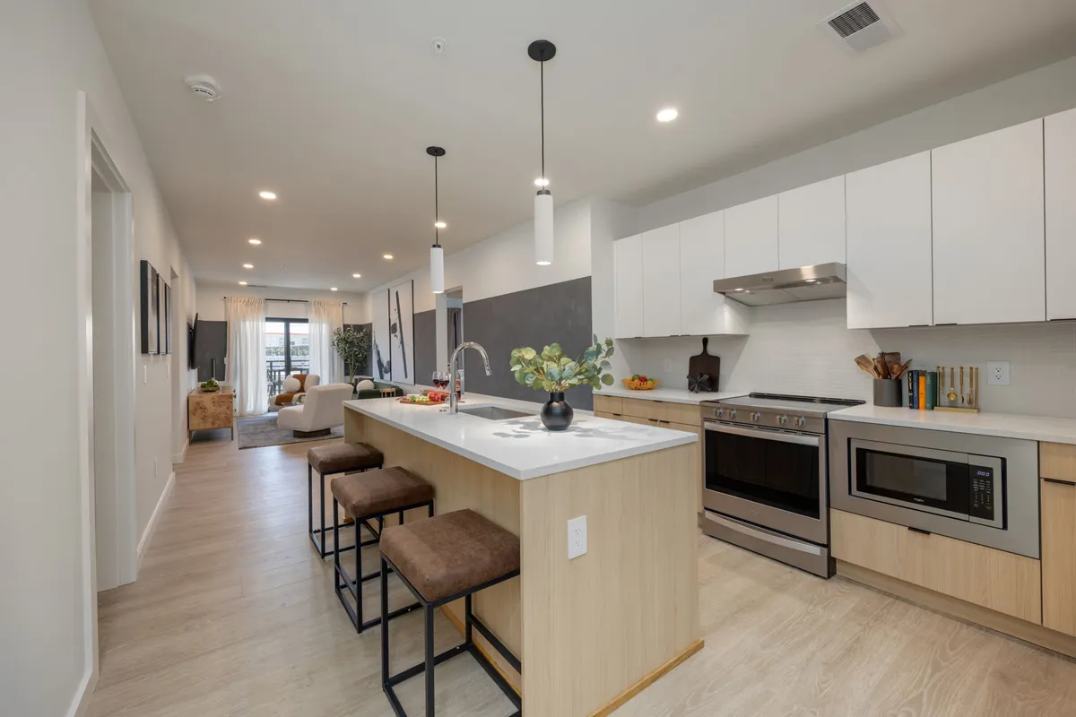 A close-up of the kitchen island with comfortable bar seating, gleaming stainless steel appliances, and stylish décor elements like decorative fruits and plants. The modern, inviting design exudes warmth and sophistication, ideal for cooking and gathering with friends or family.