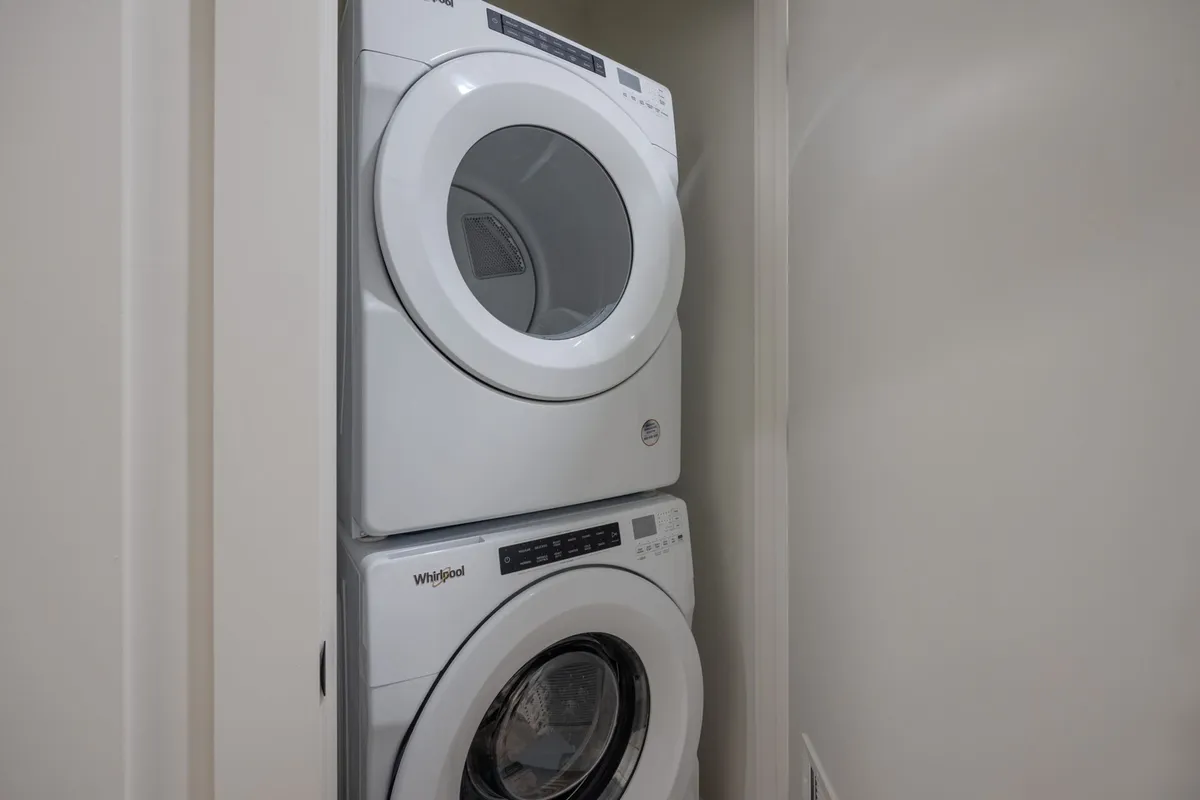 A stacked washer and dryer are neatly situated in a dedicated laundry nook, emphasizing convenience and efficient use of space. The setup features modern appliances and is designed for easy in-unit laundry care.