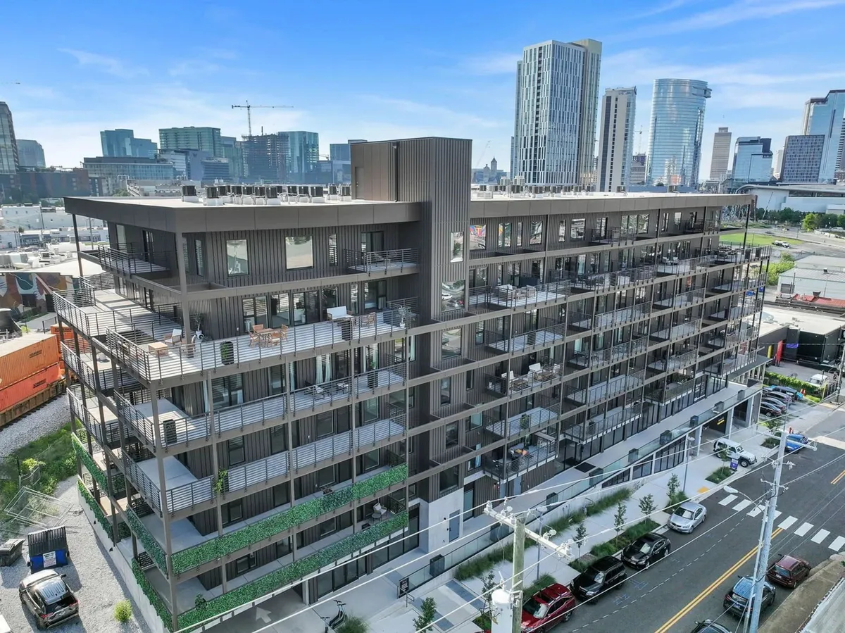 A modern building structure with balconies adorned with greenery stands prominently against a vivid city skyline. The image captures the vibrancy of urban living and the excitement of being in a central location, with the building's contemporary design and communal balcony spaces hinting at both the convenience and social atmosphere.