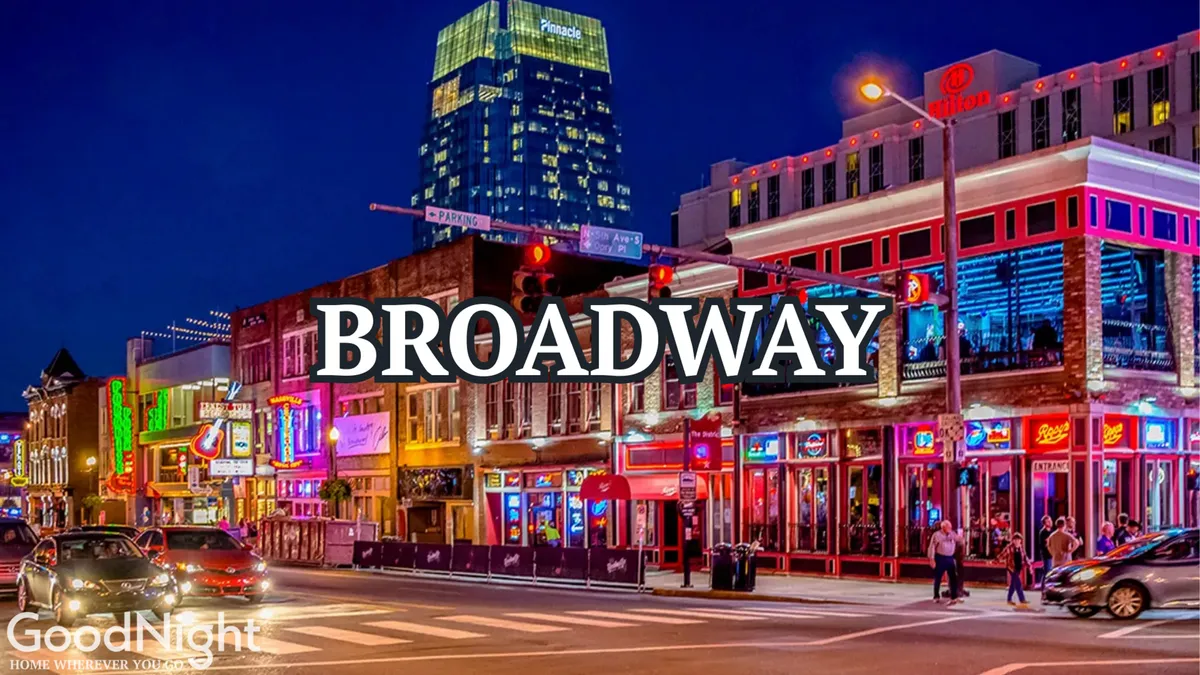 A lively nighttime streetscape in downtown Nashville, bustling with people, neon signs, and vibrant city lights. The street is filled with crowds enjoying nightlife, suggesting the dynamic and energetic heart of the city just outside the residence.