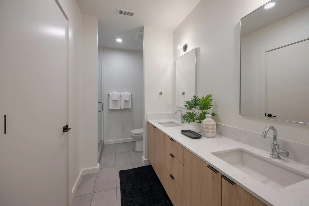 A modern bathroom featuring a vanity with sink, mirrors, a shower area, and neatly arranged towels. The color palette is clean and the space exudes a spa-like ambiance.